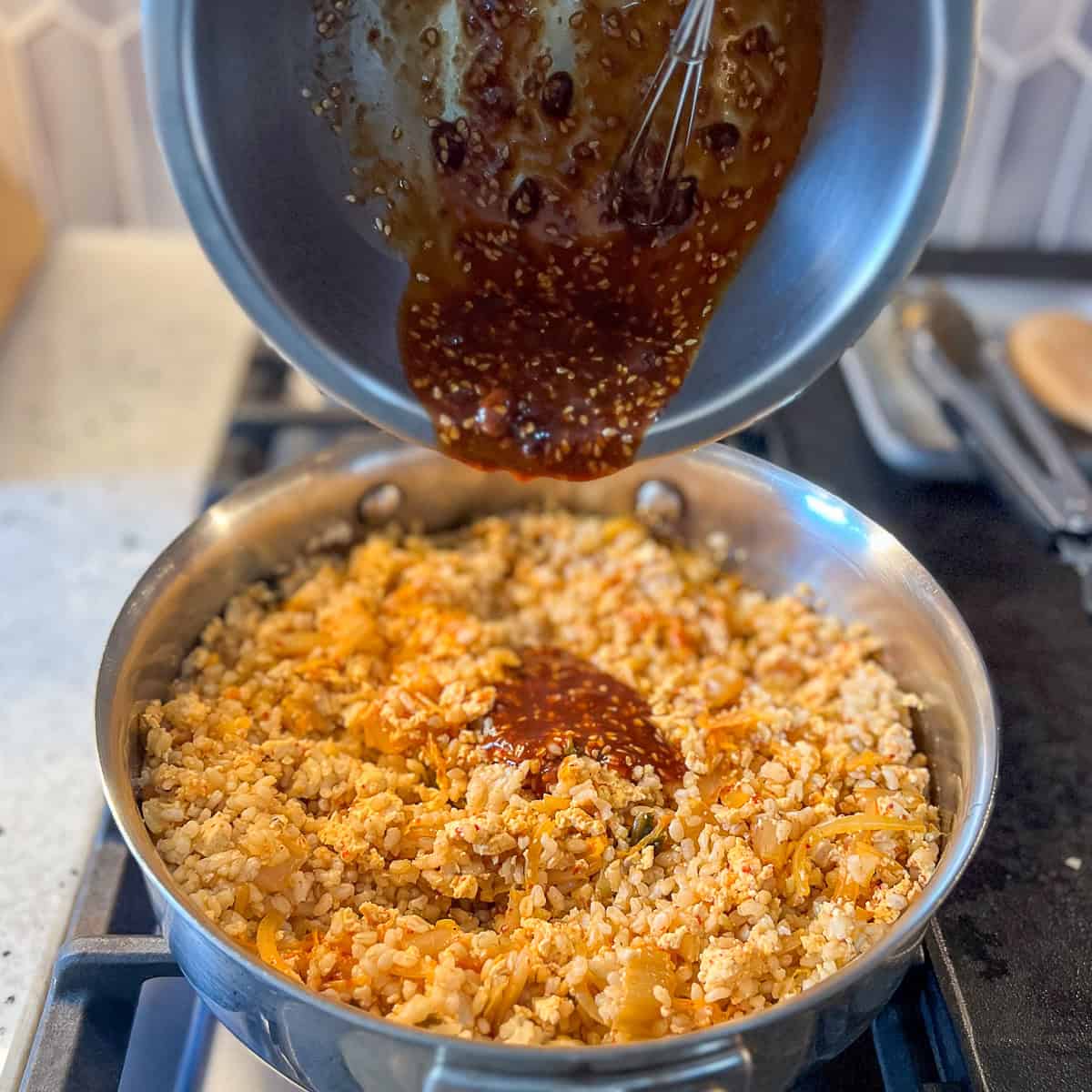 Kimchi fried rice sauce being added to the pan with rice, tofu and veggies.