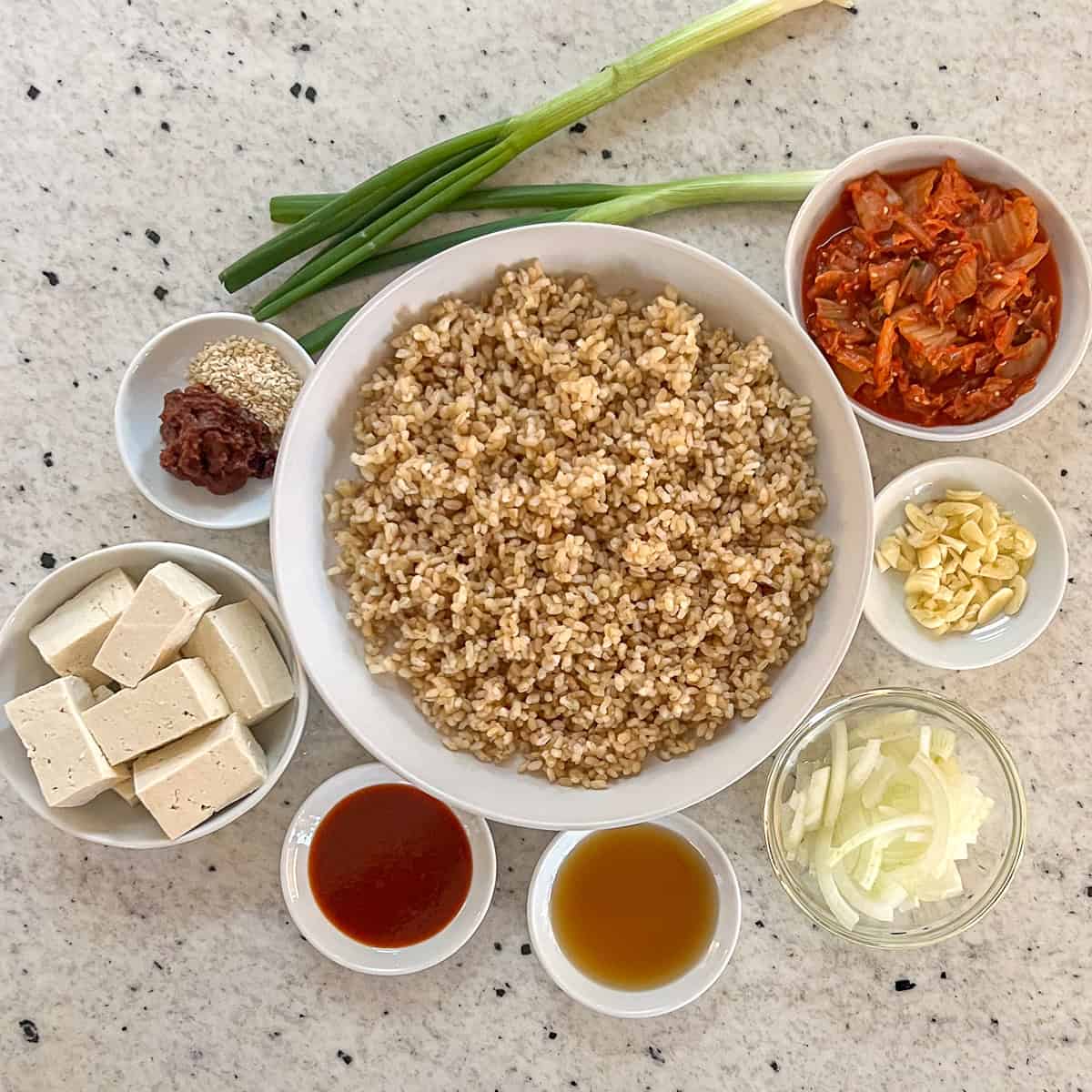 Kimchi fried rice ingredients: short grain brown rice, tofu, green onion, gochujang, soybean paste, garlic, onion, and maple syrup.