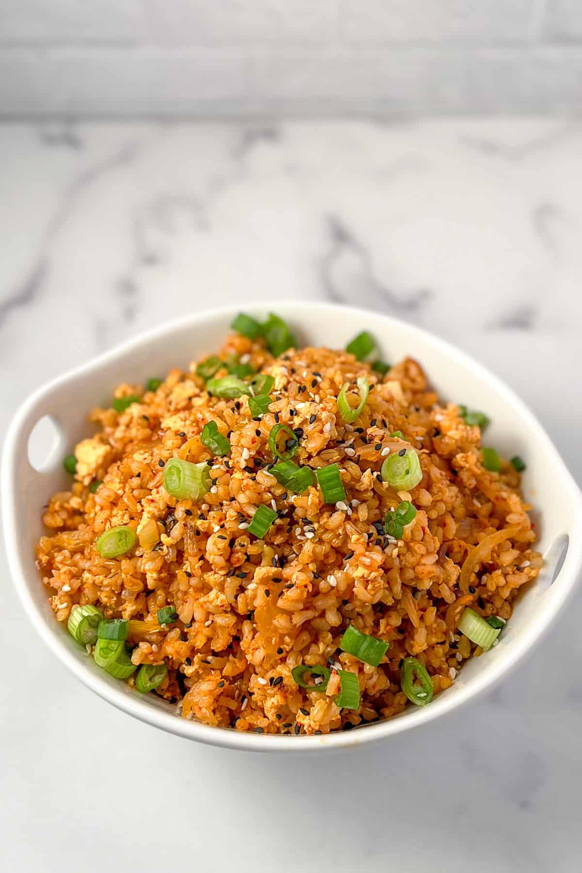 Vegan kimchi fried rice in a bowl topped with chopped green scallions.