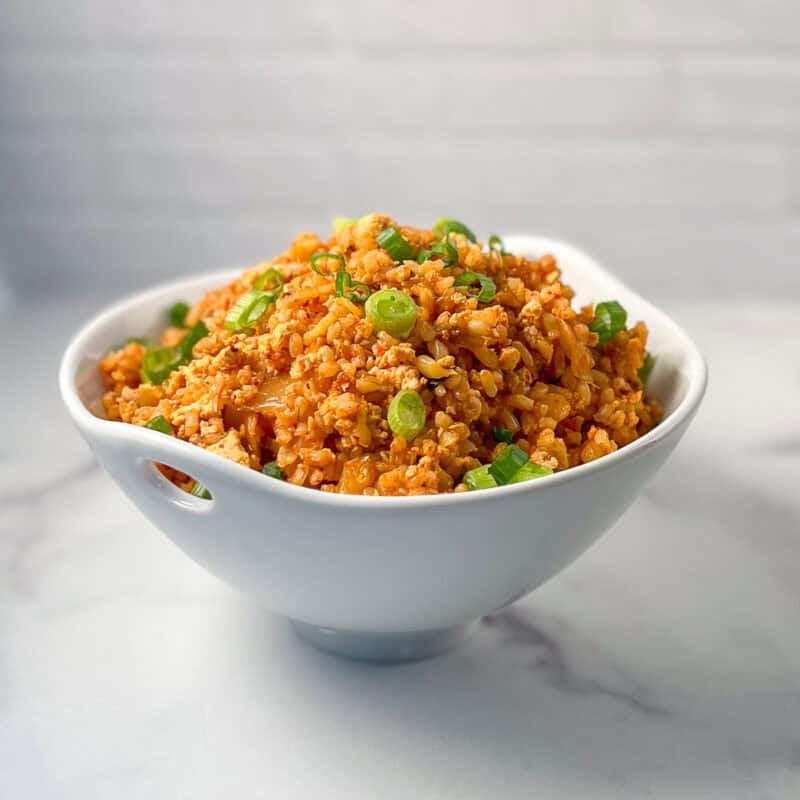 Vegan kimchi fried rice in a bowl topped with chopped green onions.