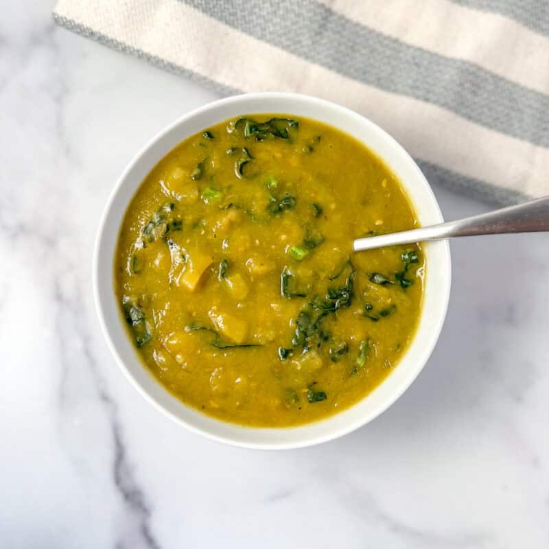 A bowl of split pea and kale soup with a spoon and napkin.