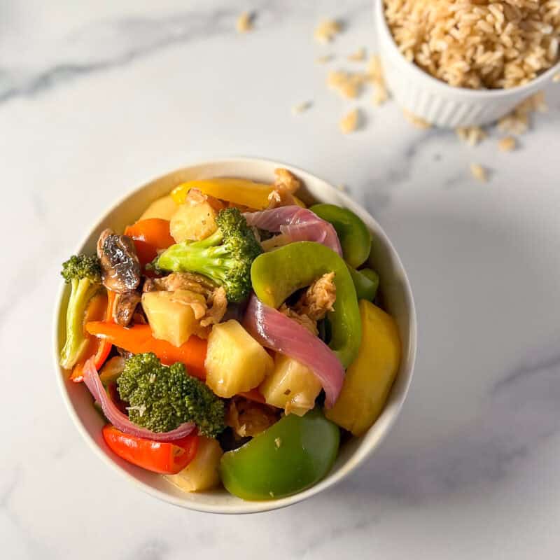 Sweet and sour vegan chicken with soy curls in a bowl, with brown rice on the side.