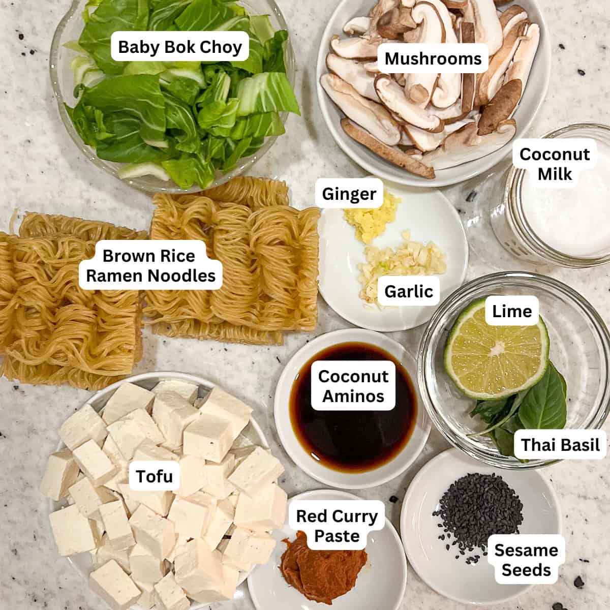 Ingredients for curry ramen: ramen noodles, tofu, mushrooms, baby bok choy, ginger, garlic, coconut milk, coconut aminos, red curry paste, Thai basil, lime, and black sesame seeds.