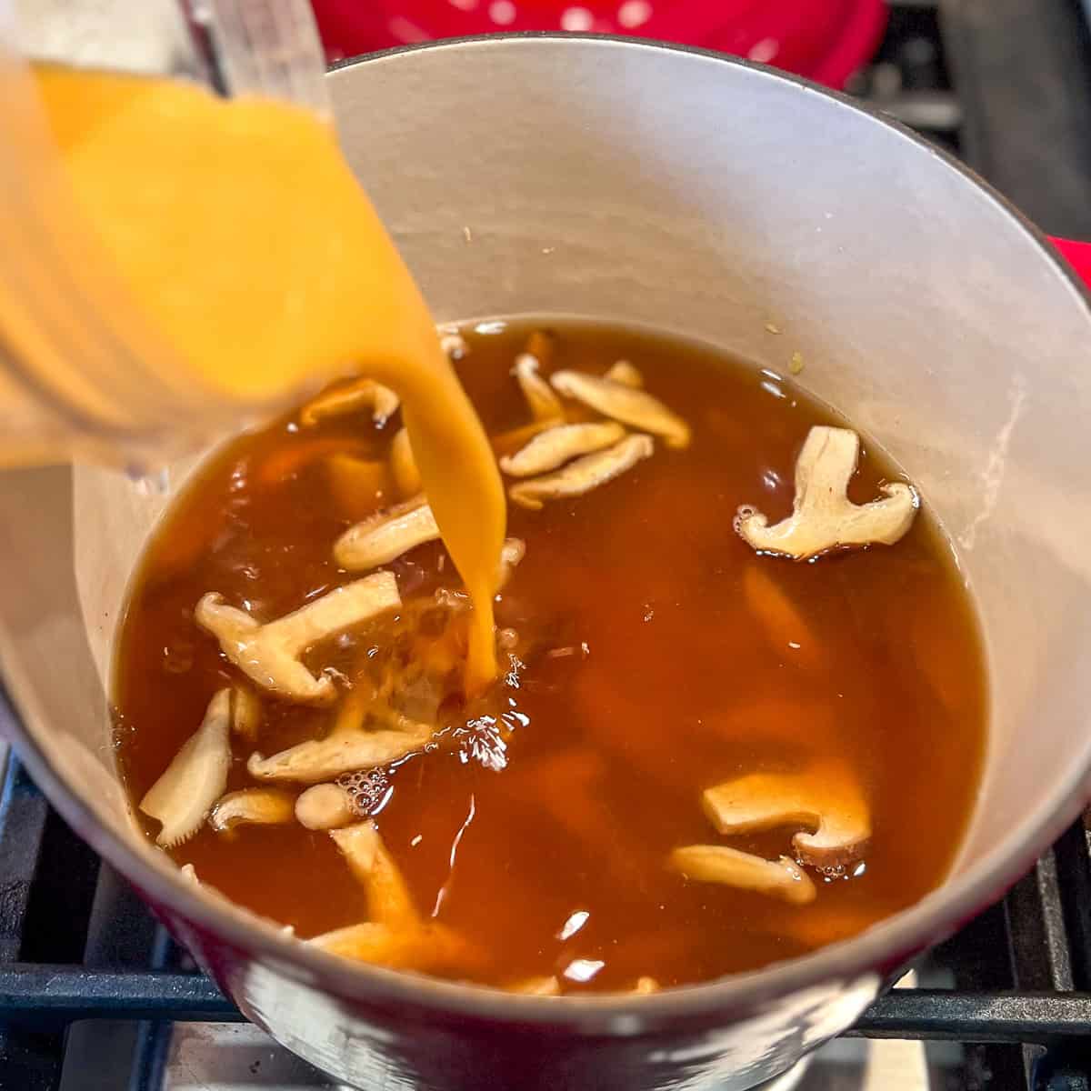 Coconut curry broth being poured into the pot with mushrooms.