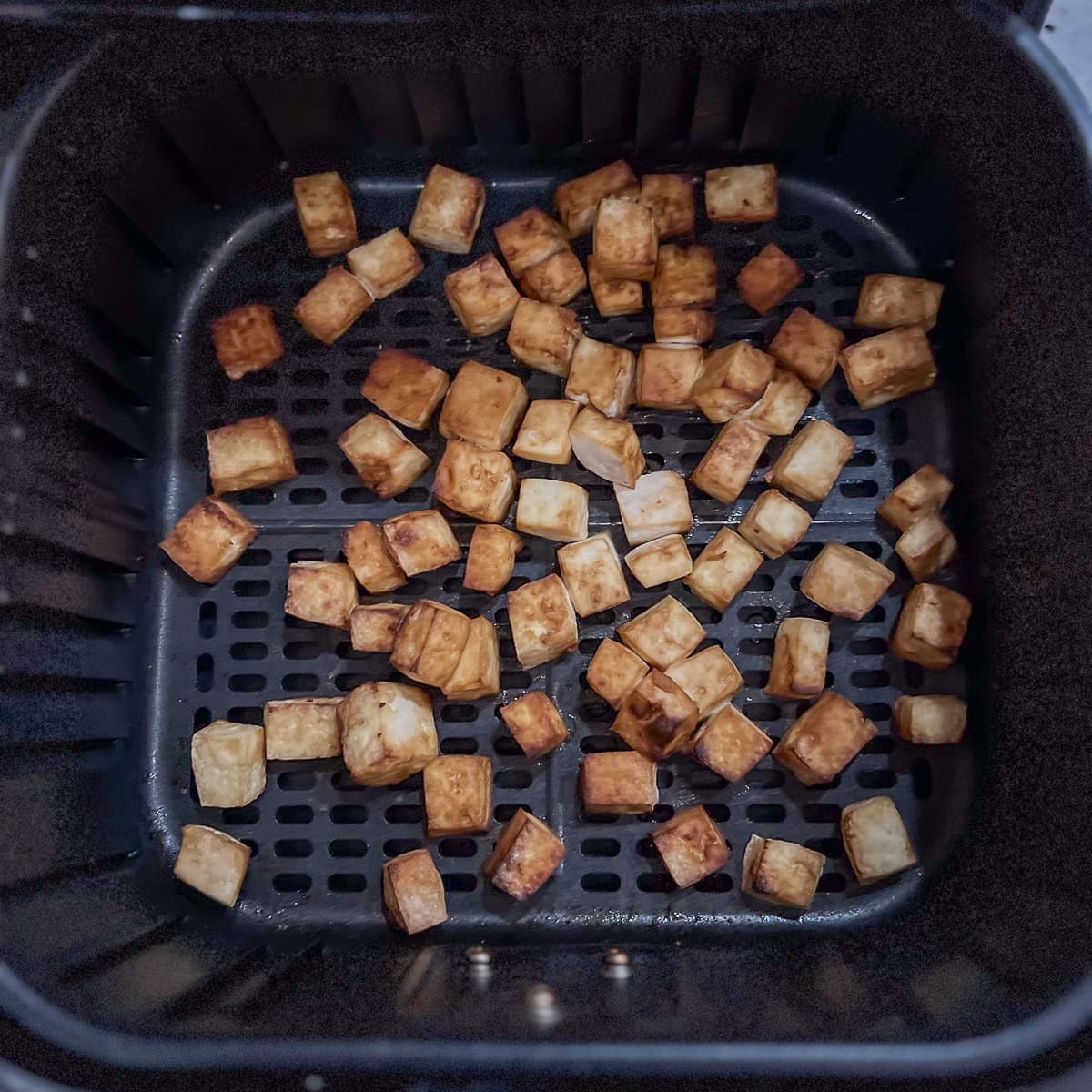 Cooked tofu chunks coming out of the air fryer.