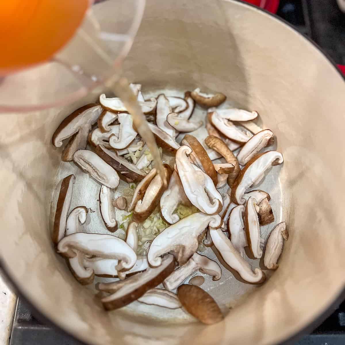 Mushrooms, garlic and veggie broth going into a soup pot.