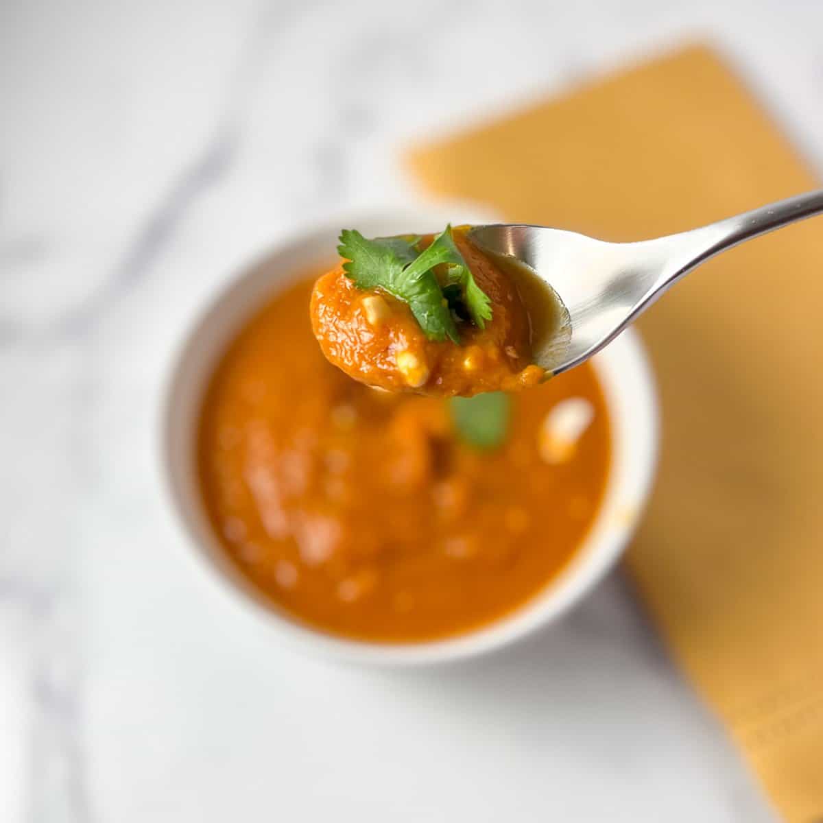 A bowl of pumpkin curry soup with a spoon lifting some out with toppings.