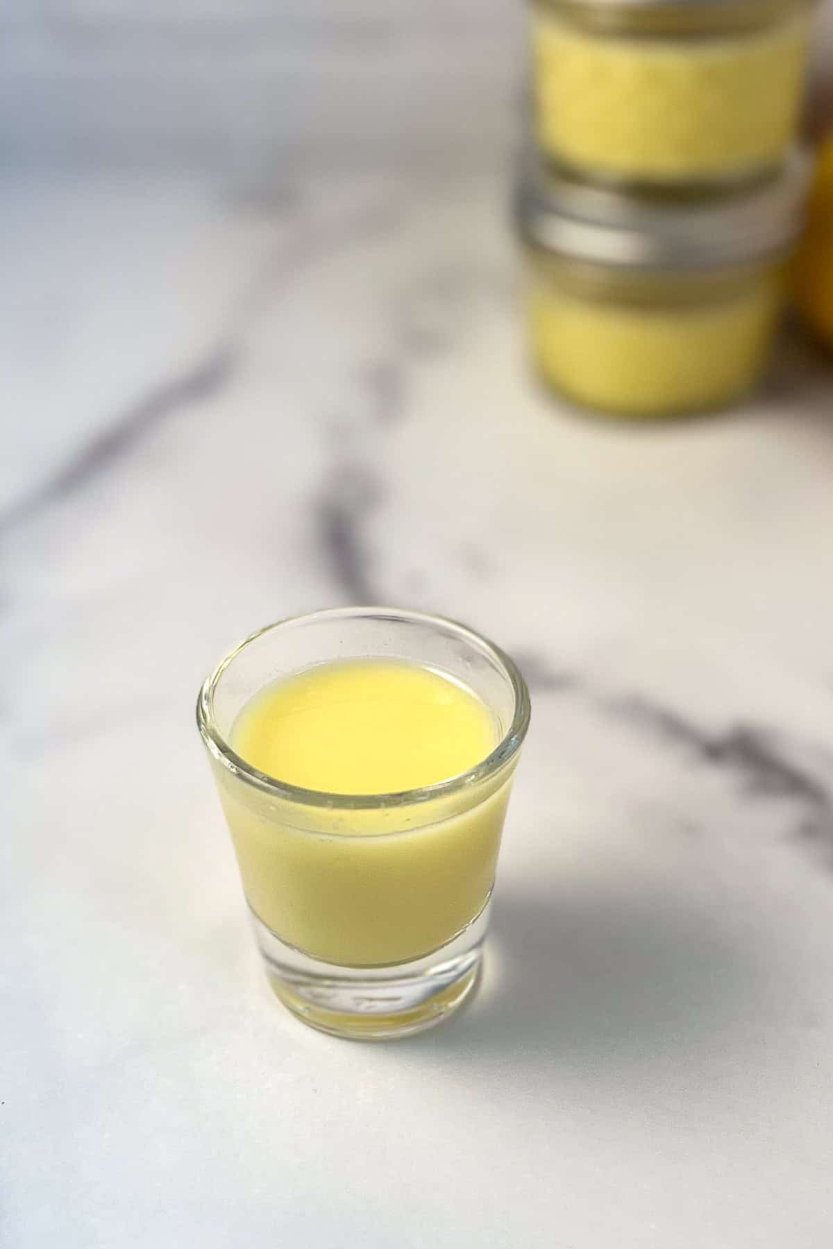 Lemon and ginger juice in a shot glass with mason jars blurred in the background.