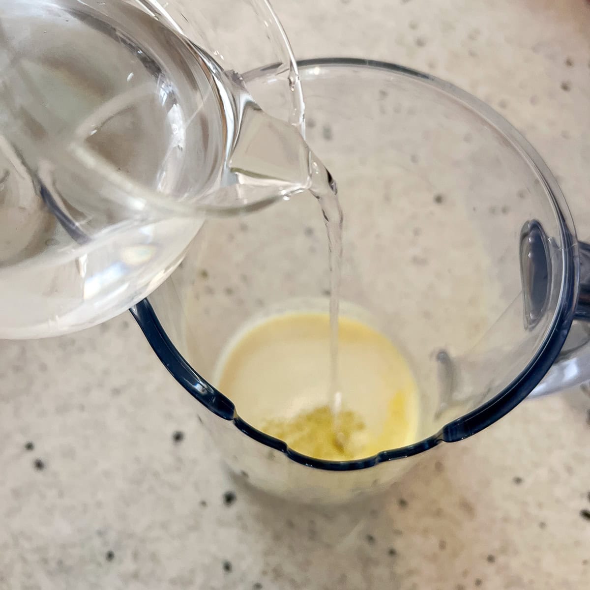 Water being poured into a pitcher with the lemon and ginger juice to dilute it.