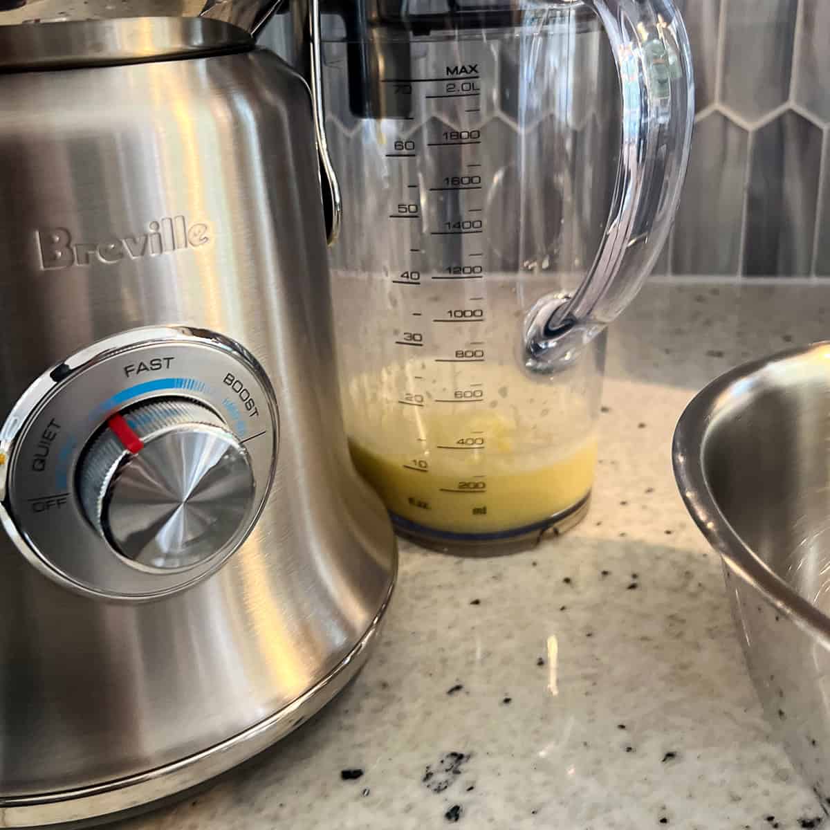 Juicer with lemon and ginger extracted juice in a pitcher.