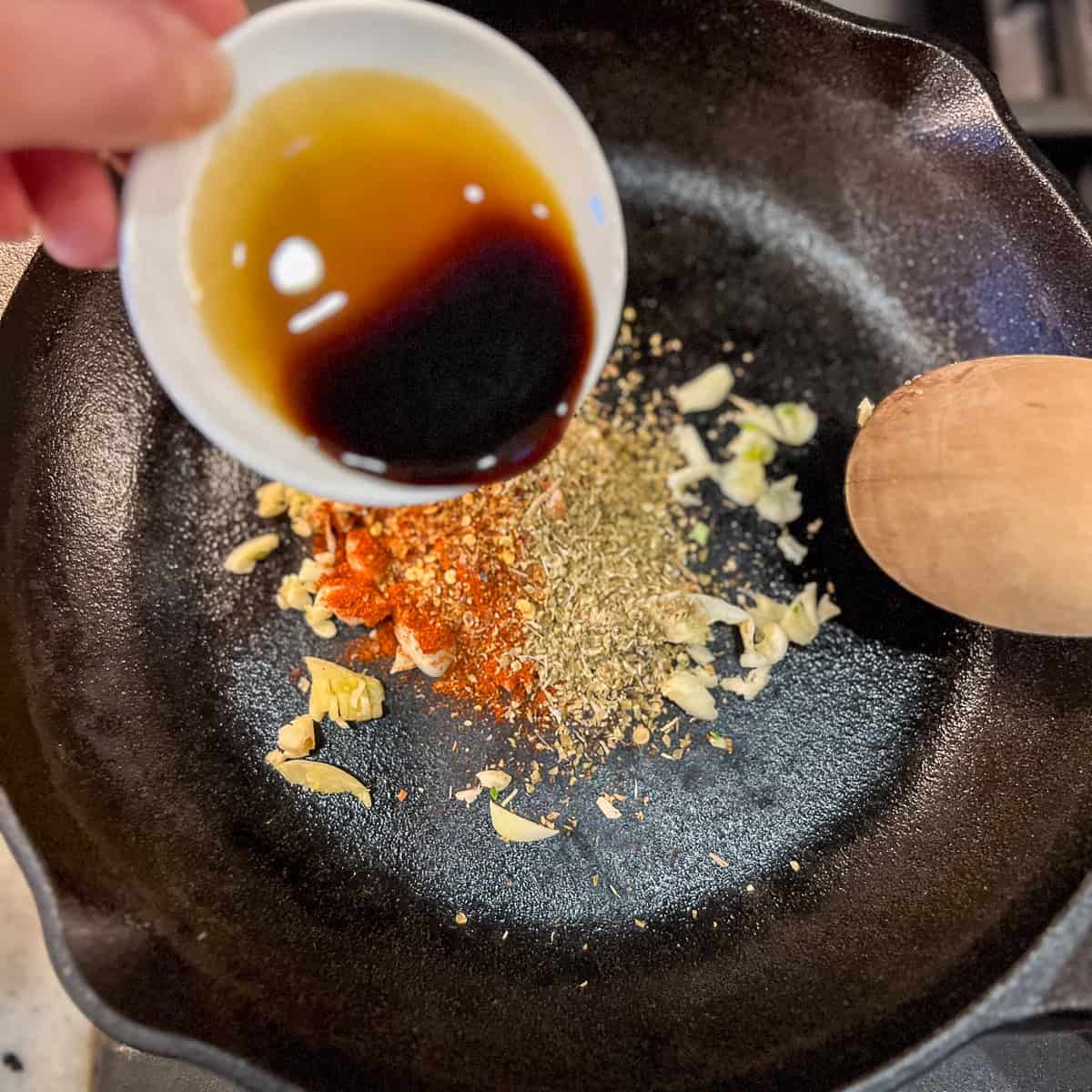 Spices and coconut aminos being added to the cast iron skillet.