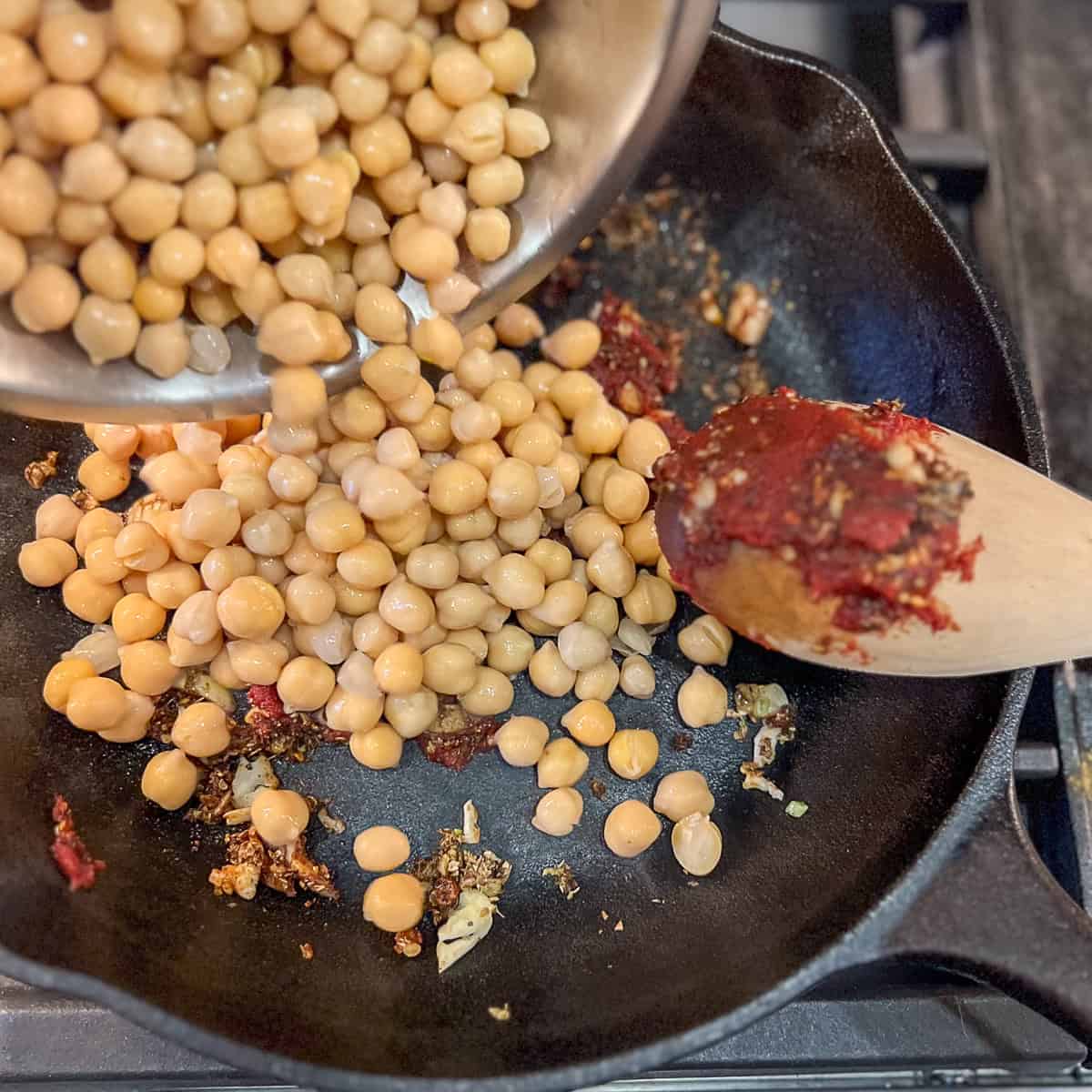 Tomato paste and chickpeas being added to the skillet.