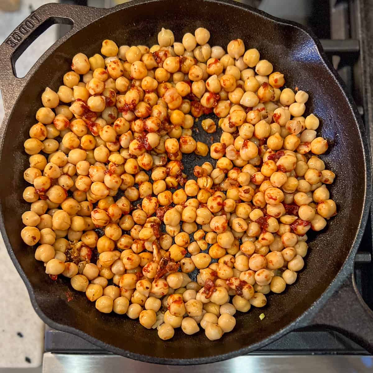 Chickpeas coated in spices and tomato paste in a skillet.