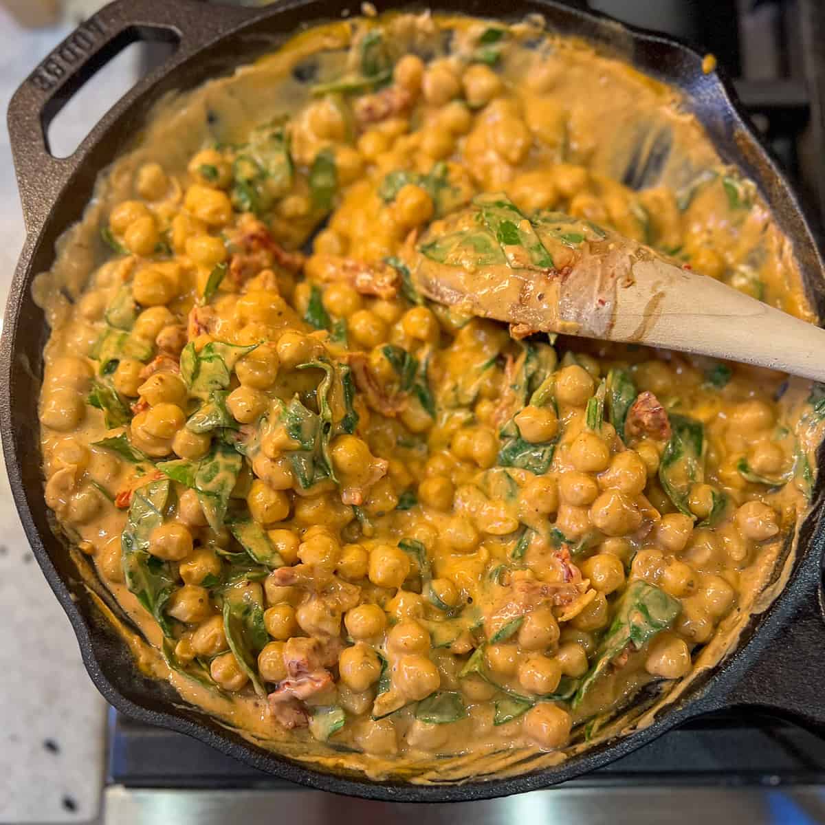 Spinach being wilted in the Marry Me Chickpeas mixture in the skillet.