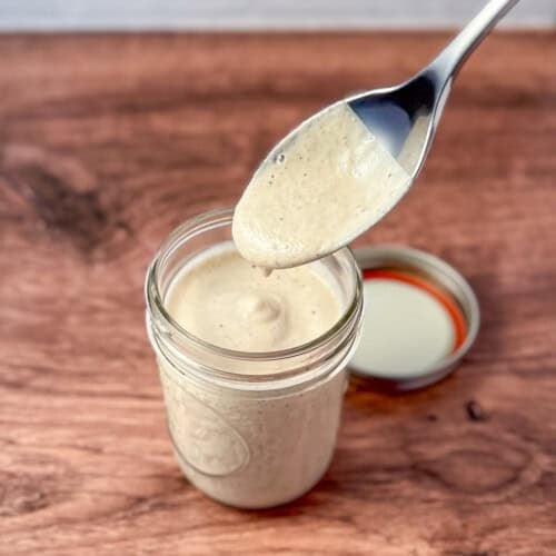 Creamy oil free Greek dressing in a mason jar with a spoon dipped in.