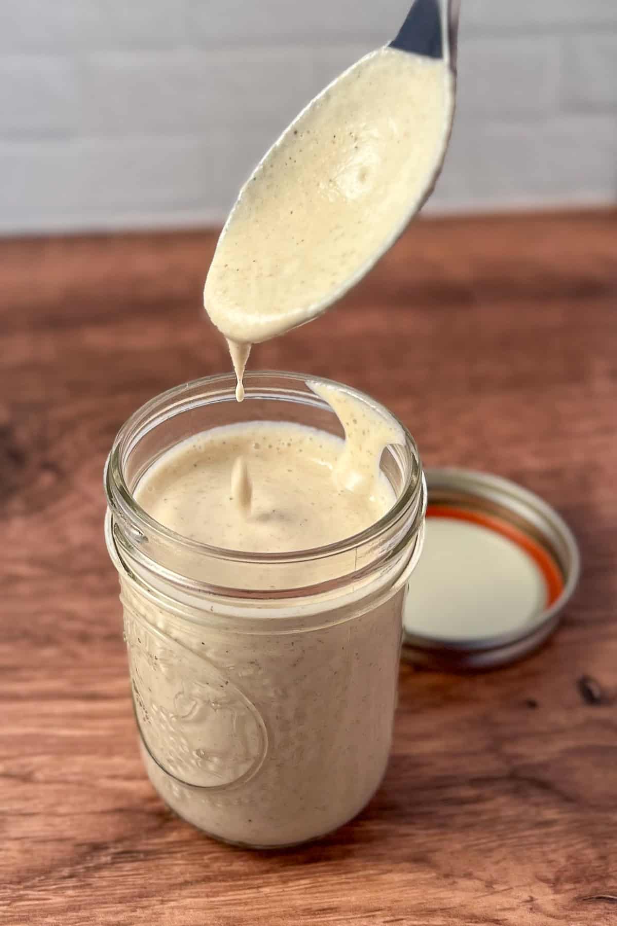 Creamy oil free Greek dressing in a mason jar with a spoon dipped in.