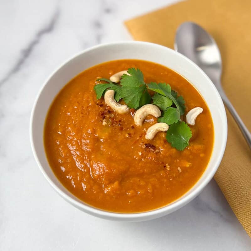 A bowl of pumpkin curry soup topped with cashews, cilantro and crushed red pepper flakes.