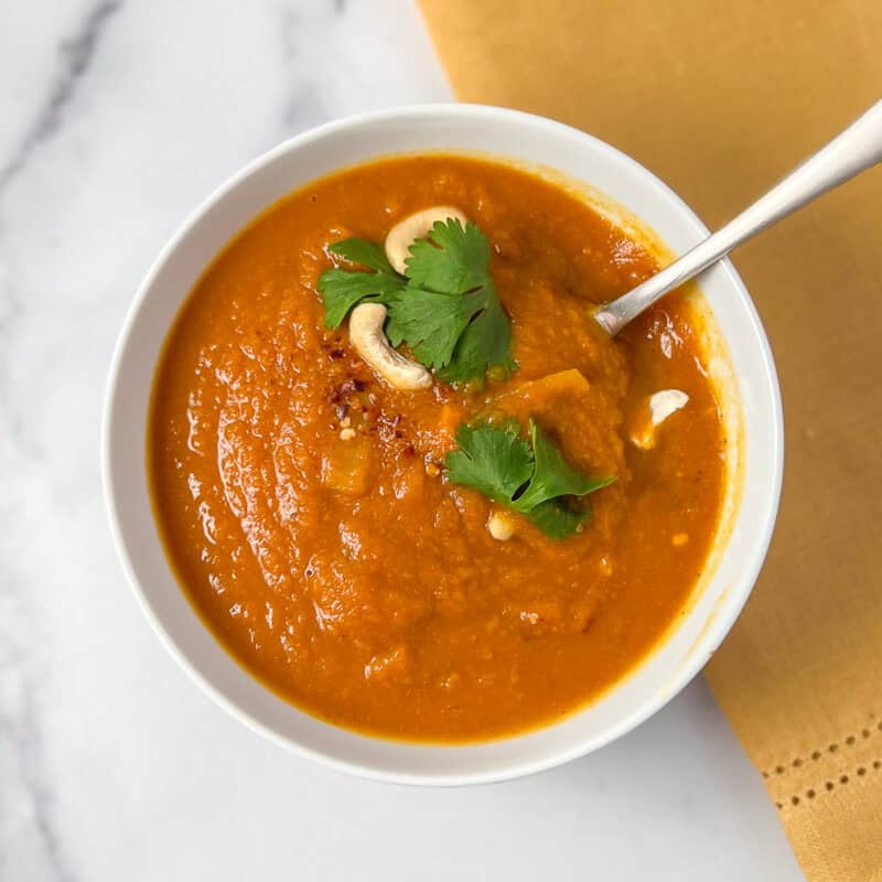 A bowl of pumpkin curry soup topped with cashews, cilantro and crushed red pepper flakes.