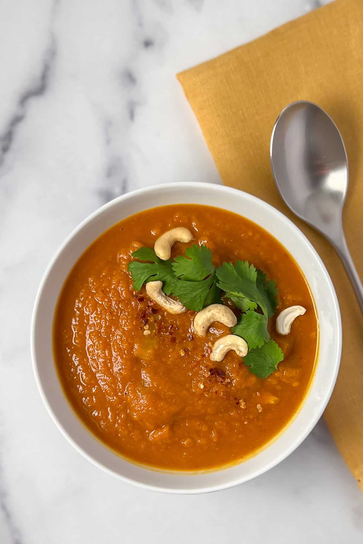 A bowl of pumpkin curry soup topped with fresh cilantro, cashews and crushed red pepper flakes.