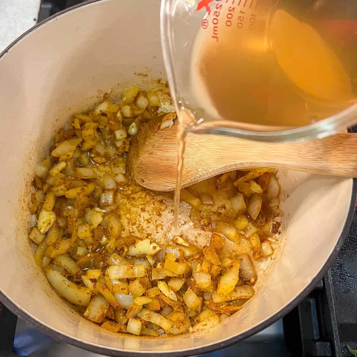 Veggie broth being poured into the pot with onions and seasonings.