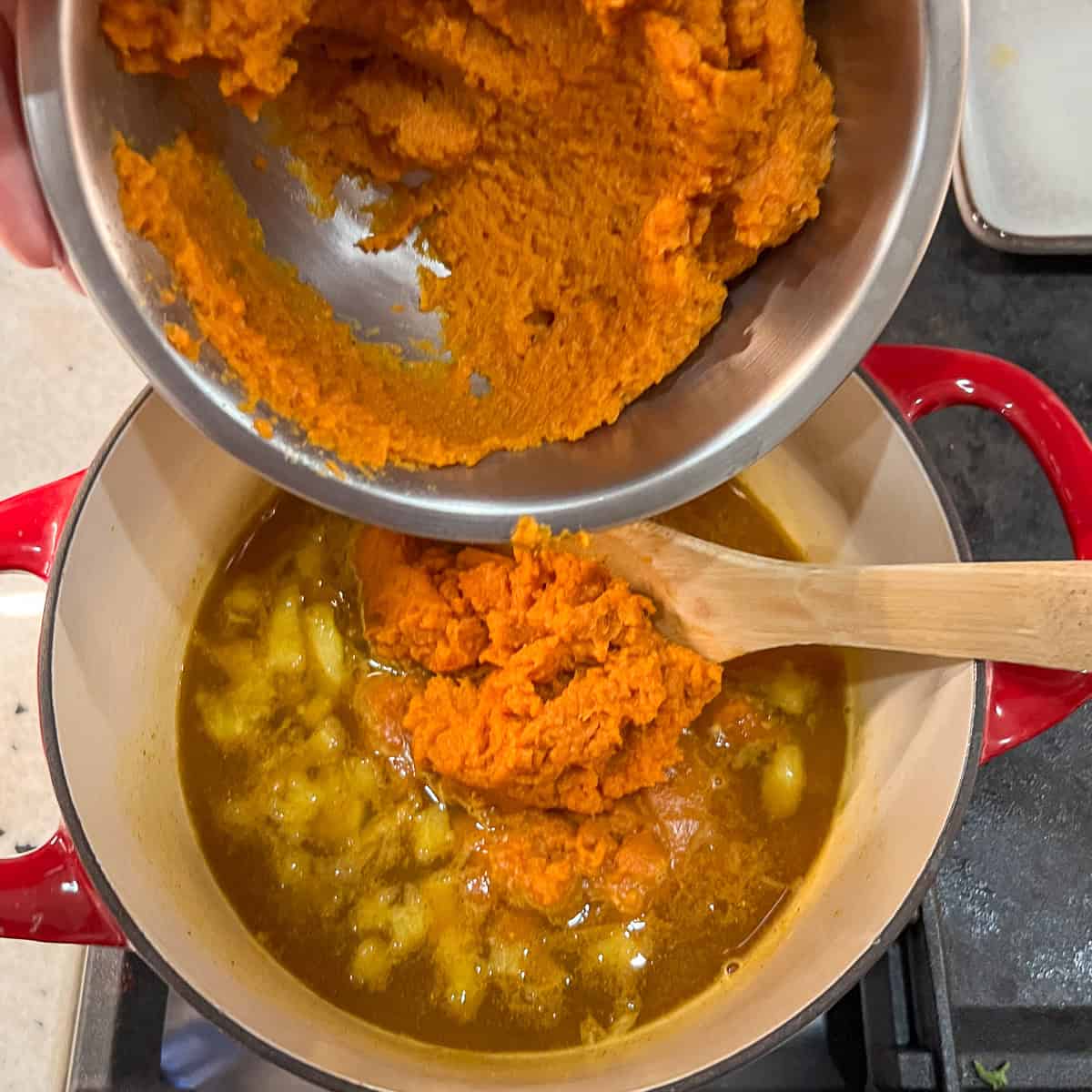 Pumpkin puree being added to the pot with vegetable broth and onions.