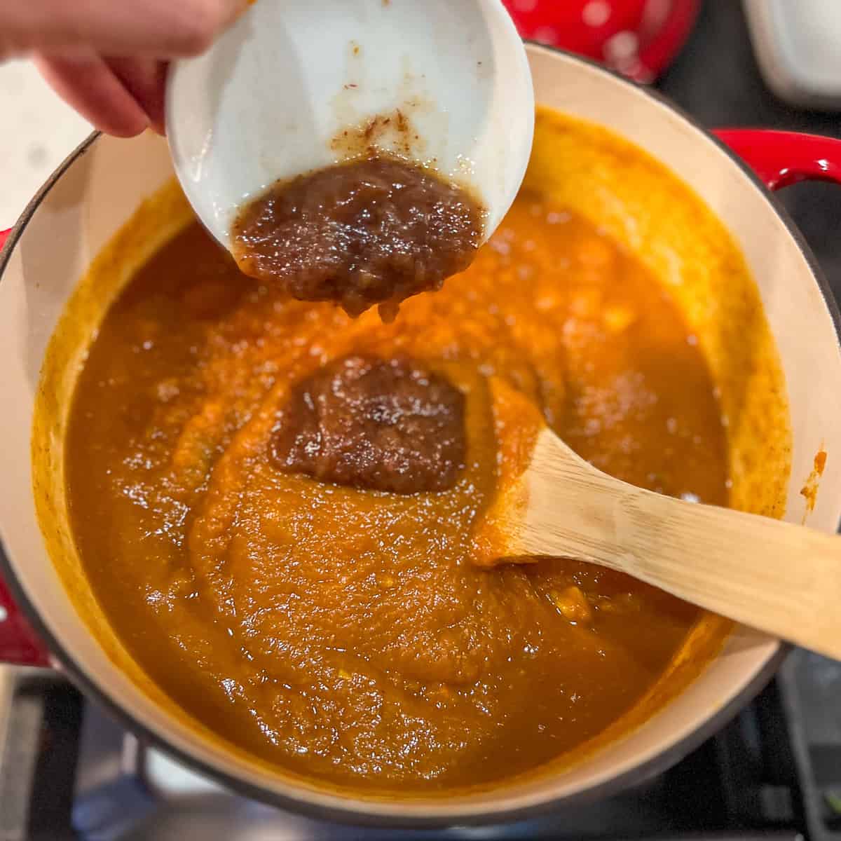 Homemade date syrup being added to the pumpkin curry soup pot.