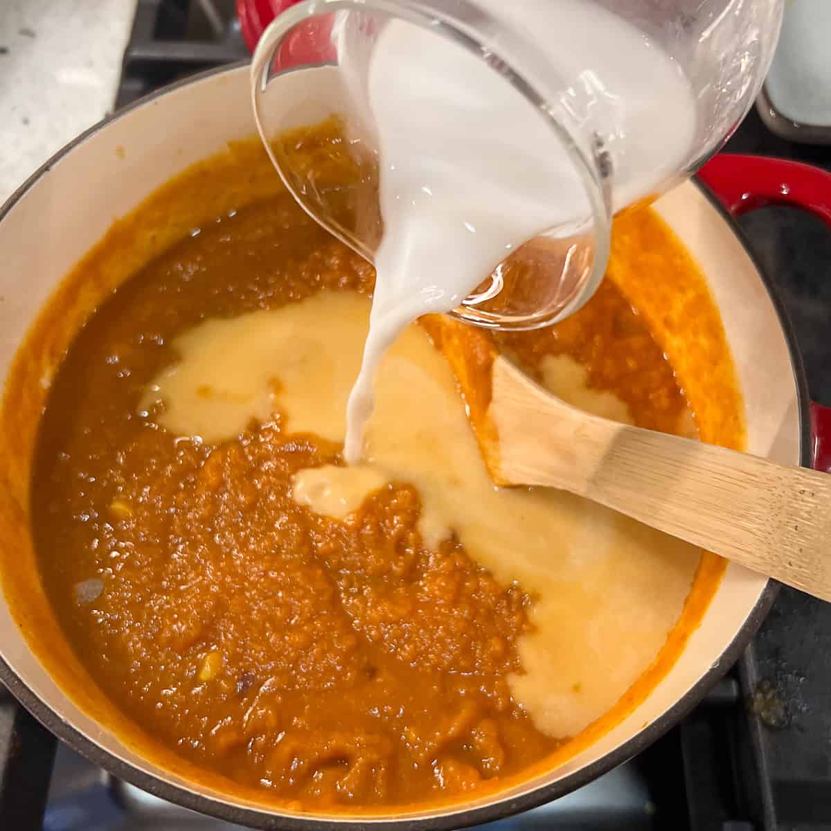 Plain unsweetened coconut milk being added to the pumpkin curry soup pot.