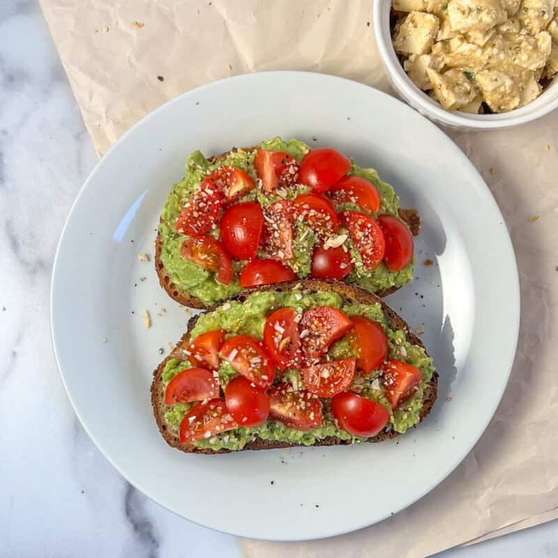 Tomato avocado toast on a plate; a dish of vegan feta cheese on the side.