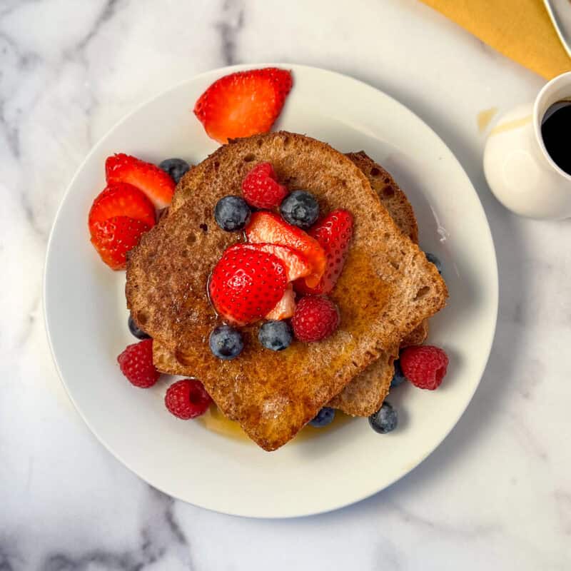 Vegan French toast on a plate topped with fresh berries and drizzled with maple syrup.