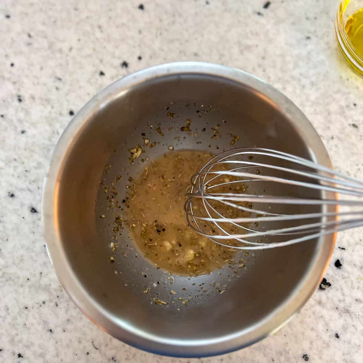 Seasonings being whisked with red wine vinegar, garlic and seasonings in a mixing bowl.