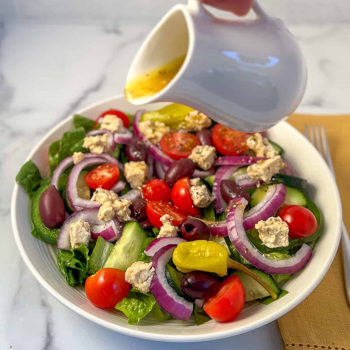 Vegan Greek salad with dressing being poured on top.