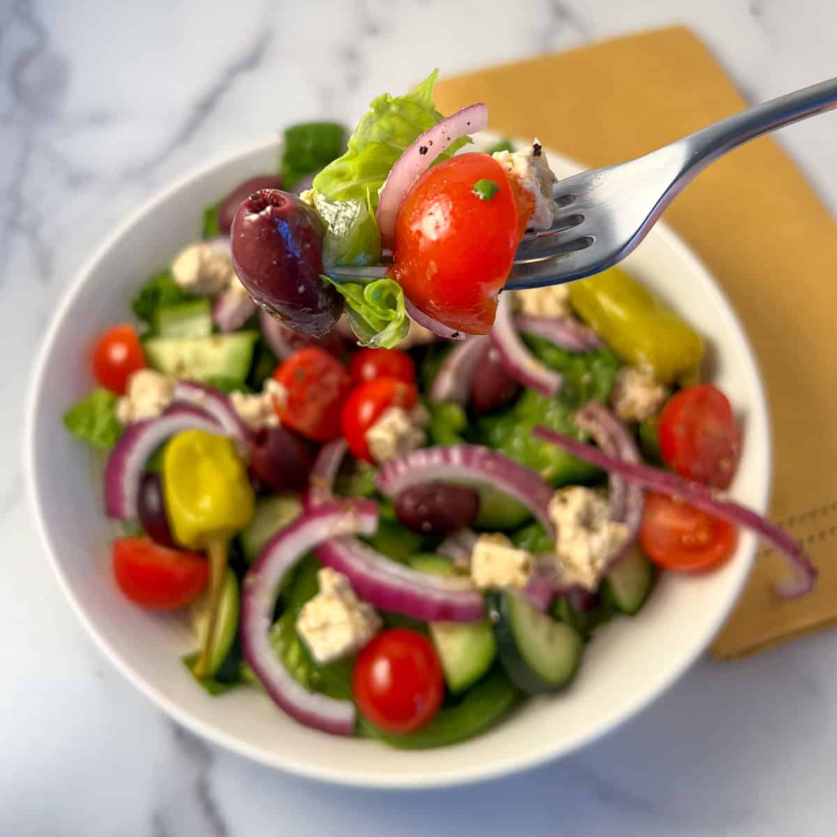 Vegan Greek salad in a bowl with fork lifting out a bite. 