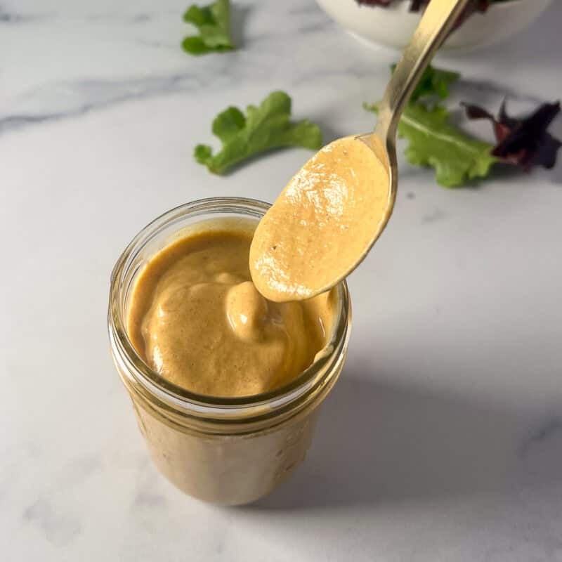 Vegan honey mustard in a mason jar with spoon dipping some out.