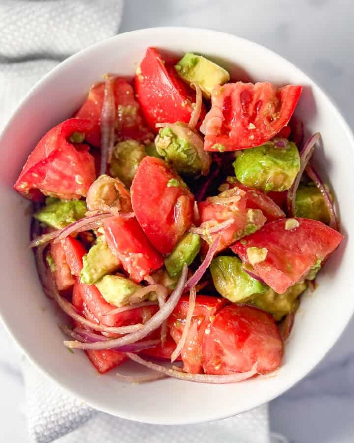 Avocado and tomato salad in a bowl with sliced red onion and lemon vinaigrette.