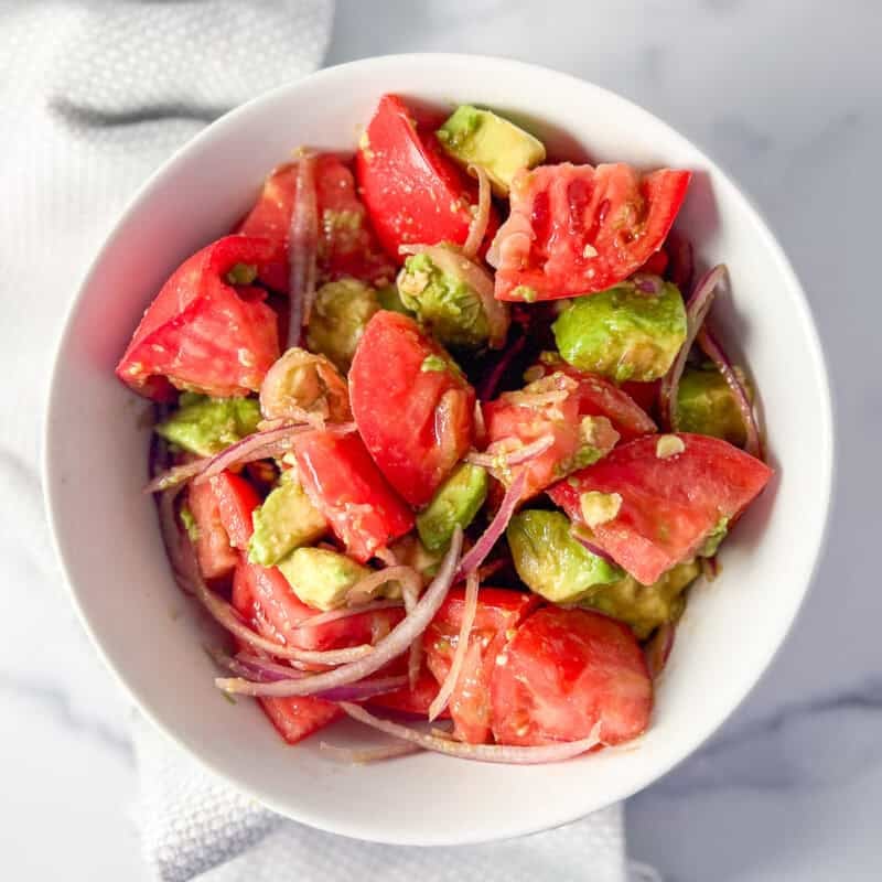 Avocado and tomato salad in a bowl with sliced red onion and lemon vinaigrette.