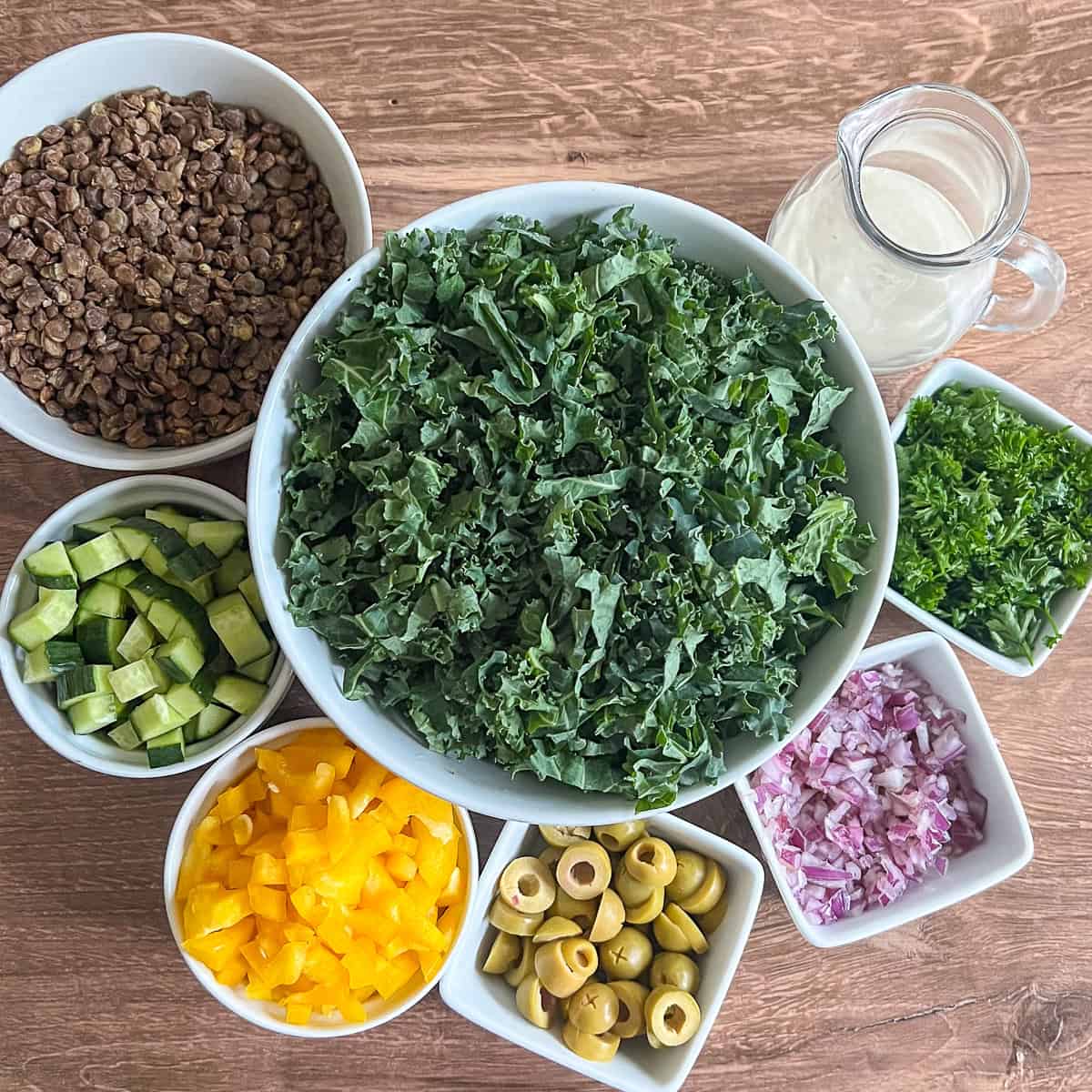 Ingredients for kale lentil salad: kale, lentils, cucumbers, bell pepper, olives, red onion, parsley, and tahini lemon sauce.