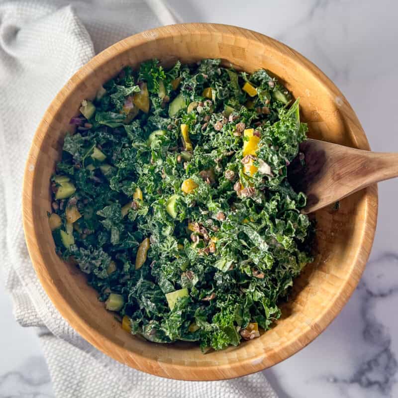 Kale lentil salad in a large wooden bowl with a wooden spoon.