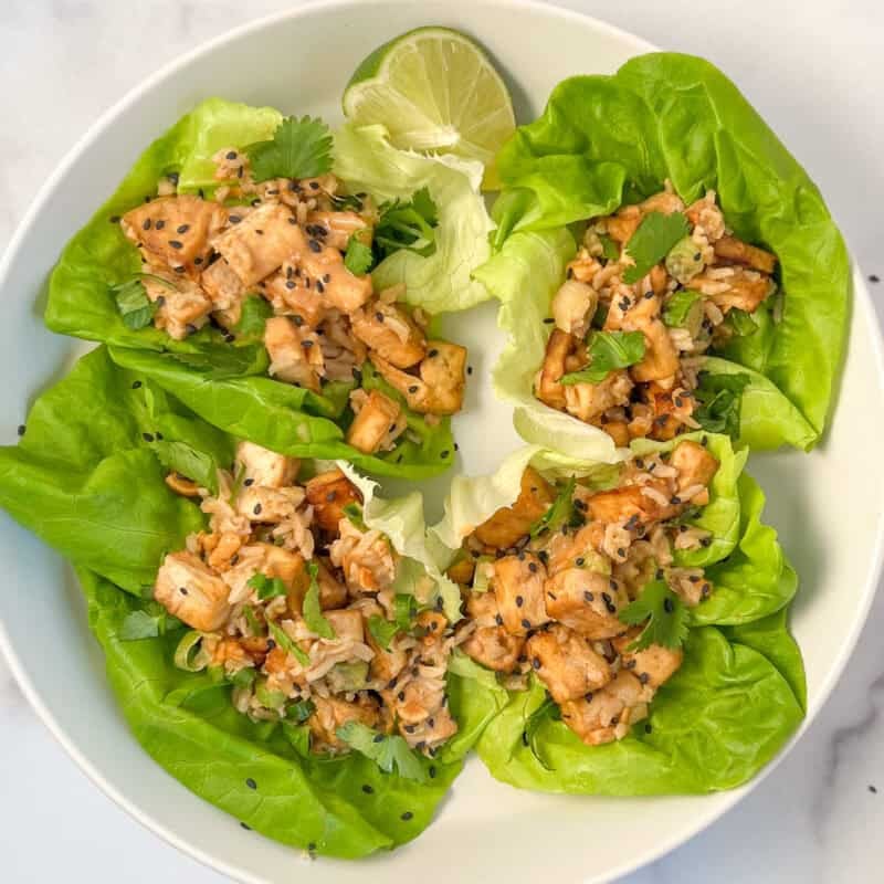 Four tofu lettuce wraps on a plate with lime wedge.