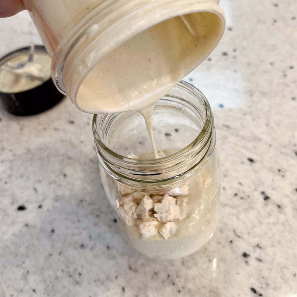 Blended dressing being added to the jar with crumbled tofu.