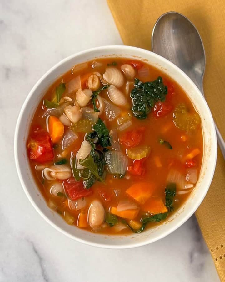 A bowl of vegan minestrone soup with a spoon on the side.