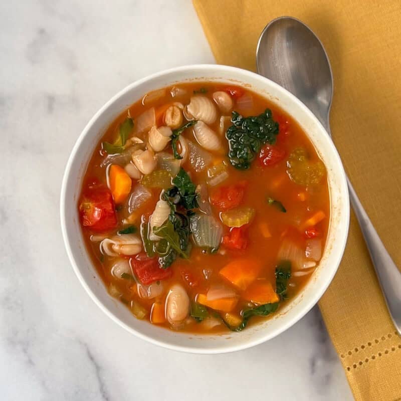 A bowl of vegan minestrone soup with a spoon on the side.