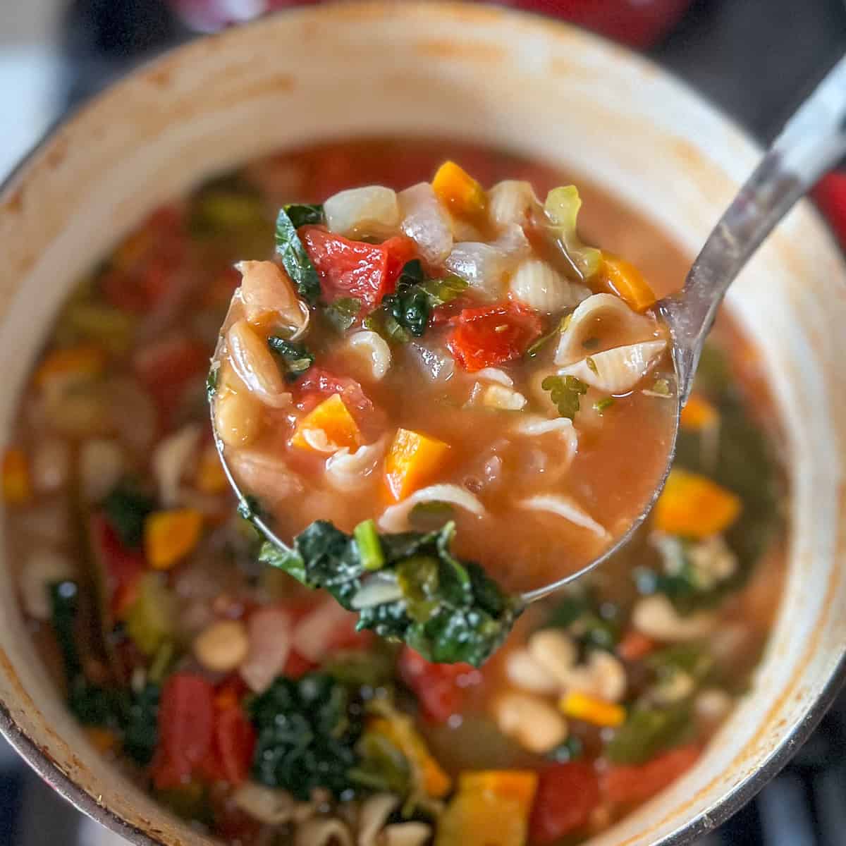 A ladle of vegan minestrone soup being lifted out of the pot.