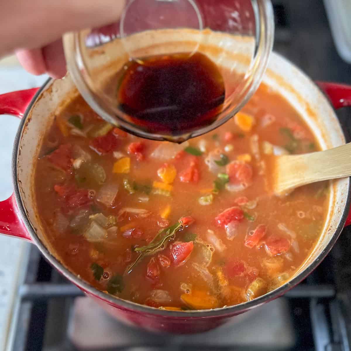 Balsamic vinegar being added to the pot of minestrone soup.