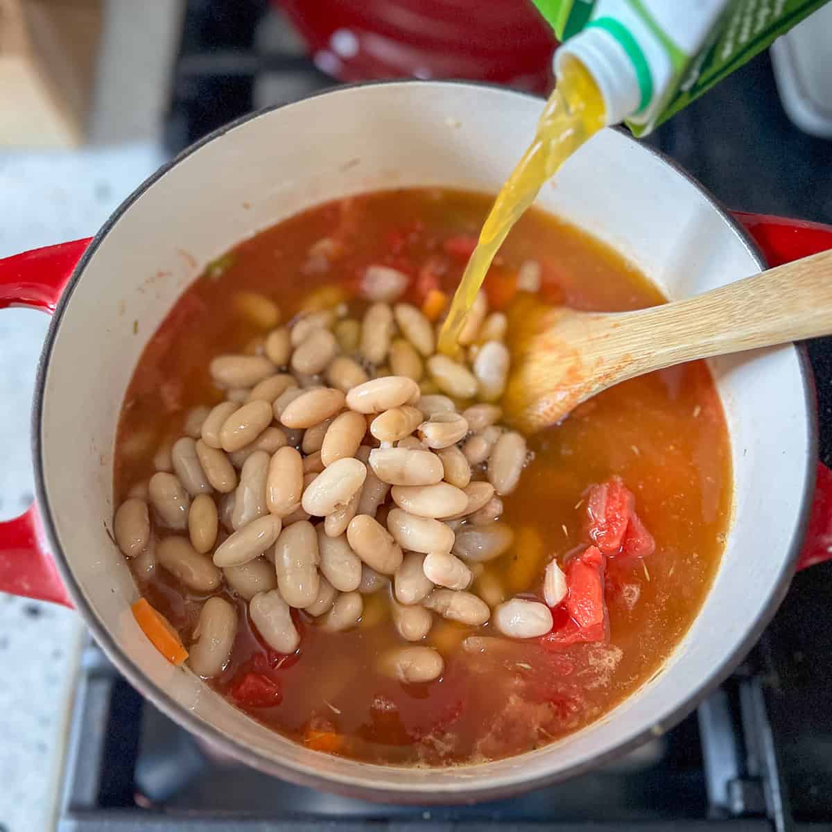 Beans, tomatoes, bay leaves, and vegetable broth being added to the pot.