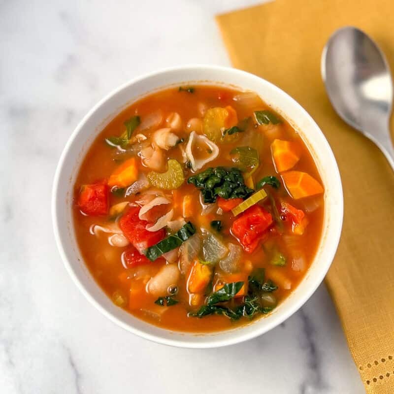 Bowl of vegan minestrone soup in a bowl with spoon on the side.