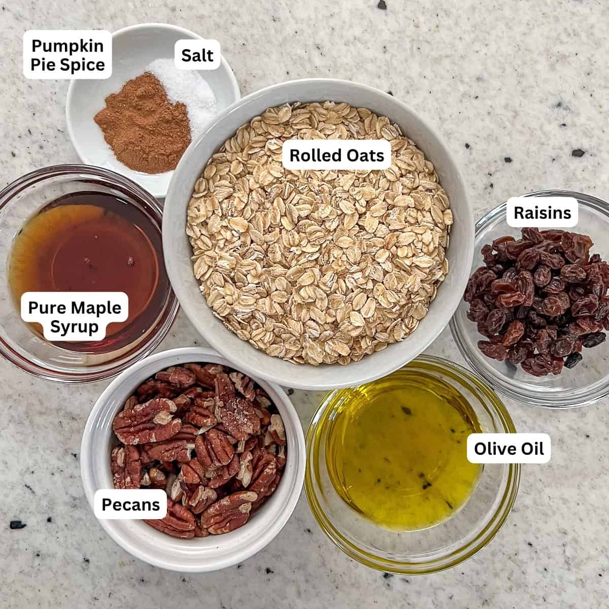 Ingredients for pumpkin spice granola: rolled oats, pecans, pumpkin pie spice, salt, maple syrup, olive oil, and raisins.
