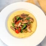 Polenta and mushroom in a bowl with cherry tomatoes and spinach.