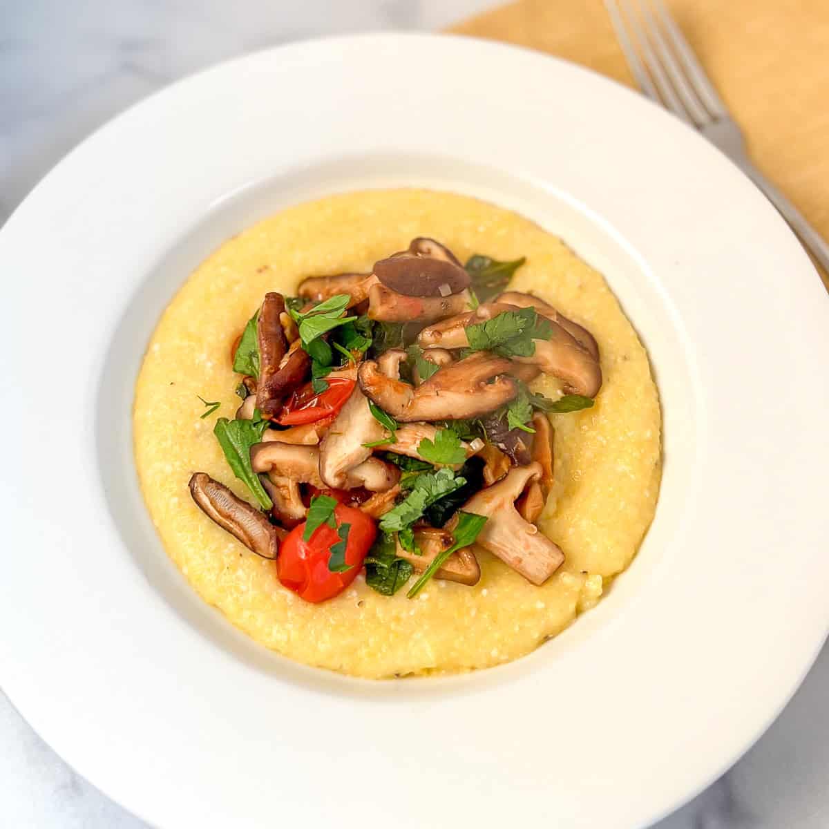 Polenta and mushroom in a bowl with cherry tomatoes and spinach.
