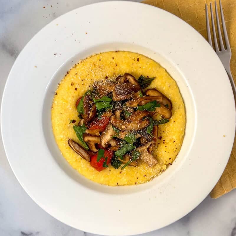 Creamy polenta and mushroom with cherry tomatoes and spinach in a bowl.