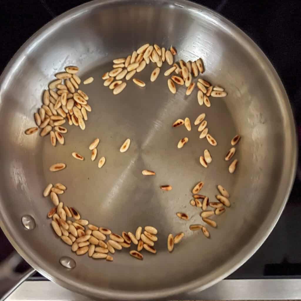 Skillet with pine nuts being toasted on the stovetop.
